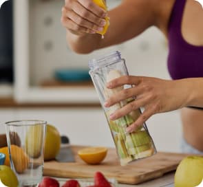 A woman in sportswear squeezing lemon juice into a bottle with fruits on a kitchen counter. 
            Other fruits and berries are placed around.
